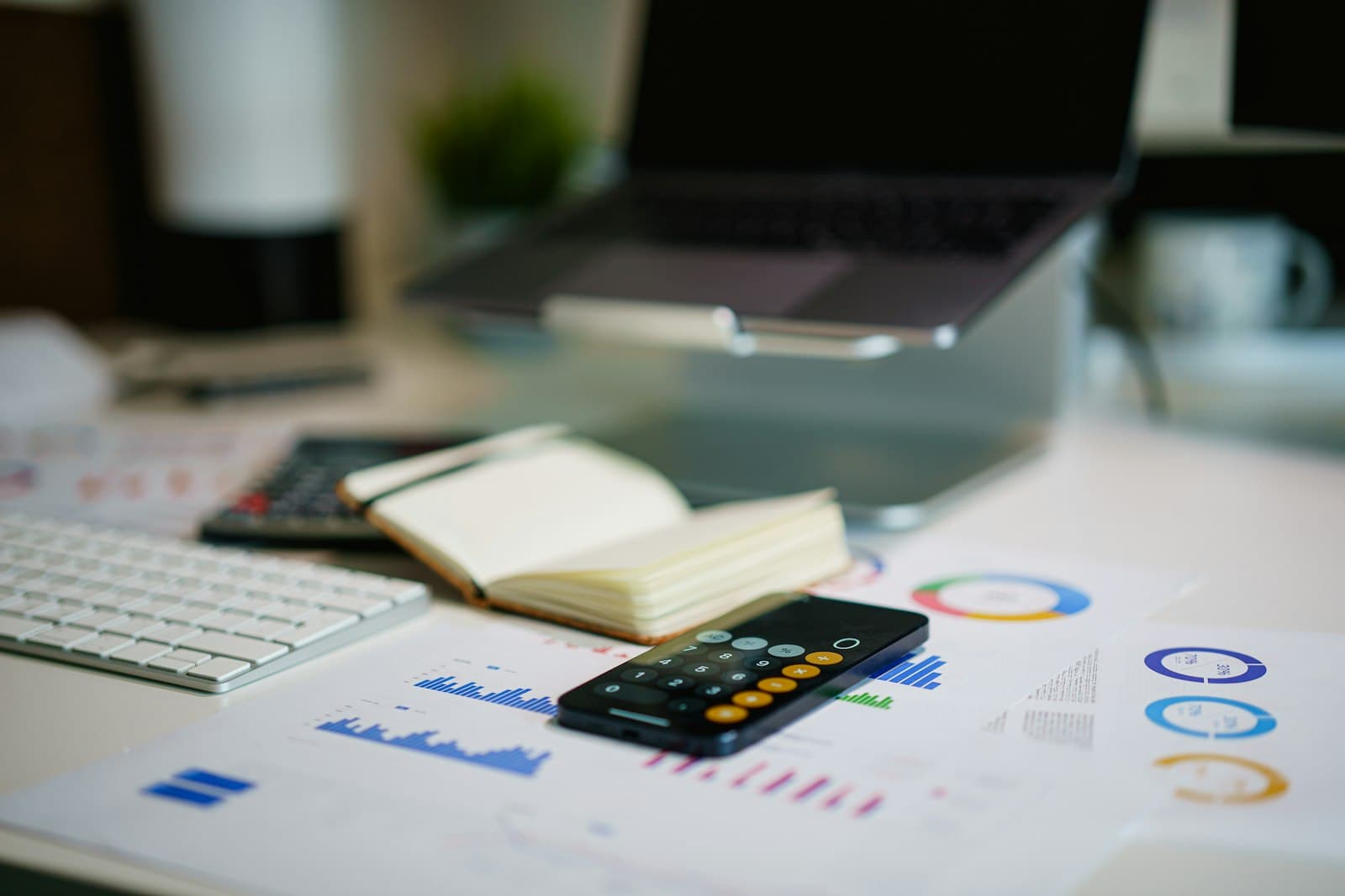 A hand pointing at rows of financial figures on a printed report next to a laptop