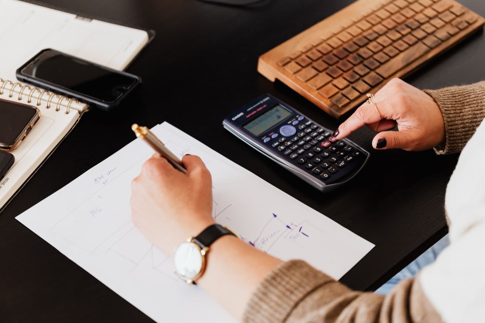 A bookkeeper using a calculator while reconciling figures on paper